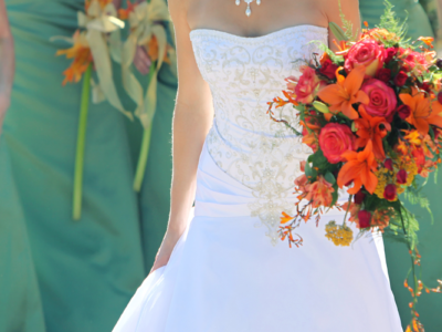 A bride in a white lace wedding dress holding her bouquet with her bridesmaids standing behind her.